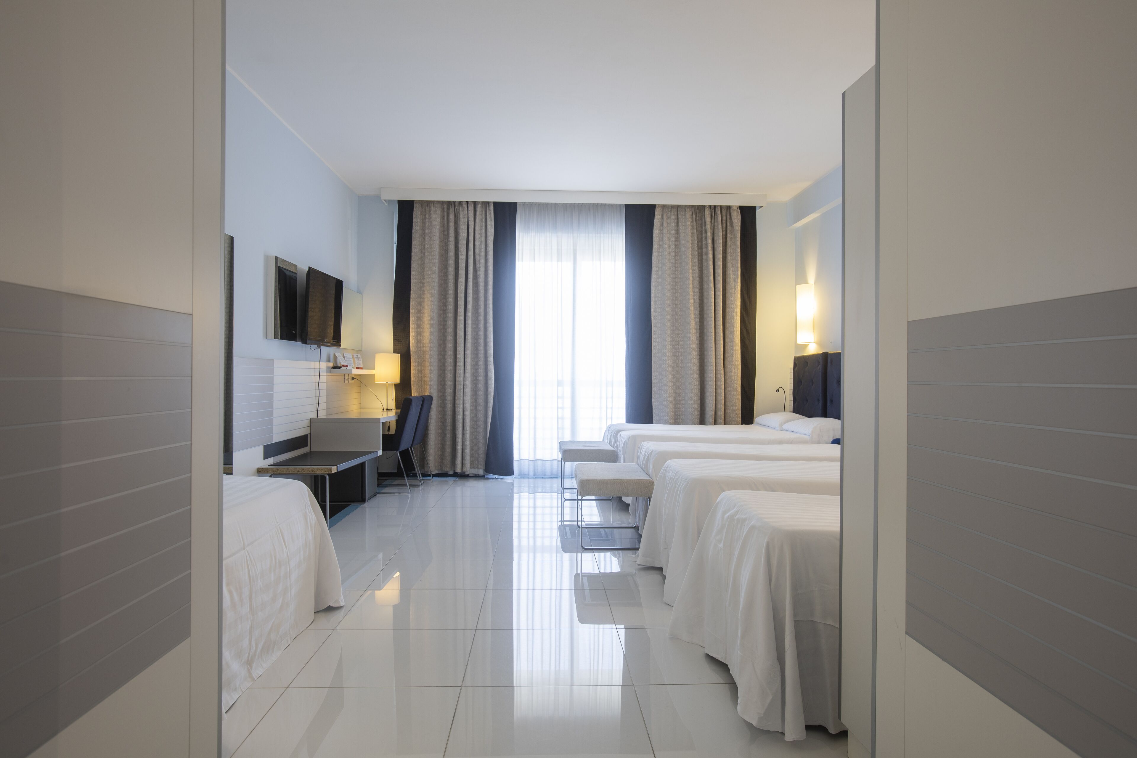 Habitación de hotel con cama, escritorio, silla y televisor en la pared.