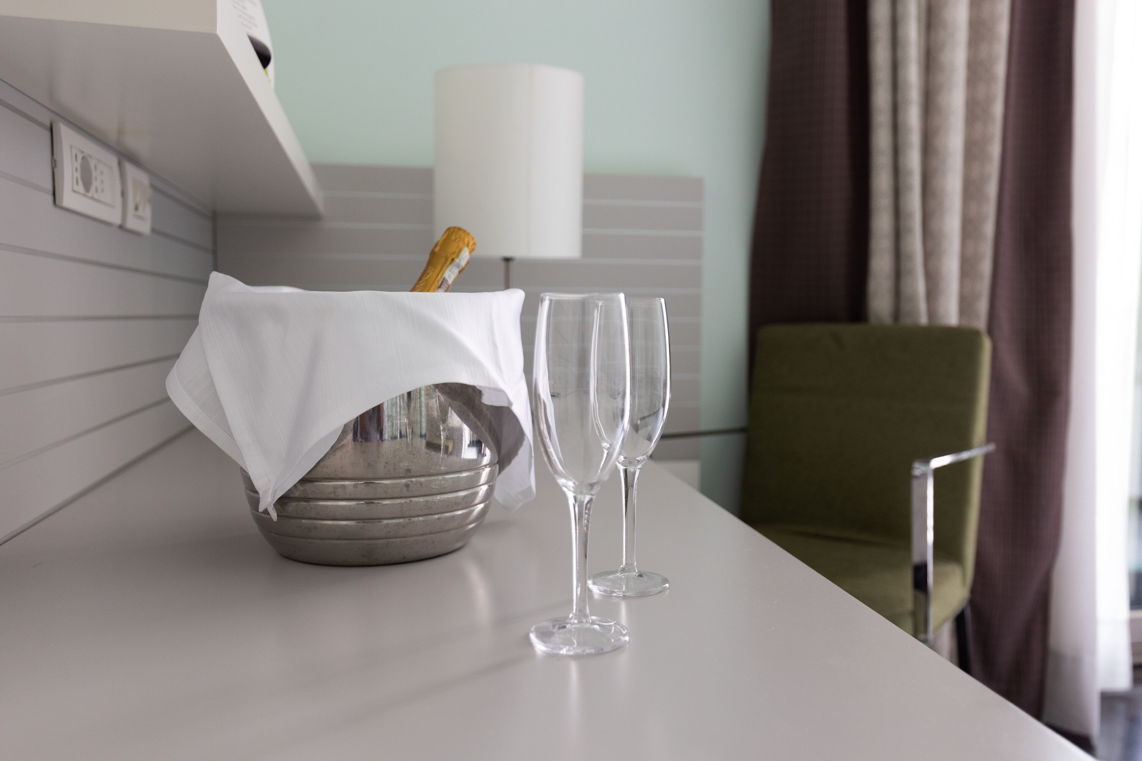 Ein Hotelzimmer mit Tisch für zwei Personen, einer Champagnerflasche und zwei Gläsern.