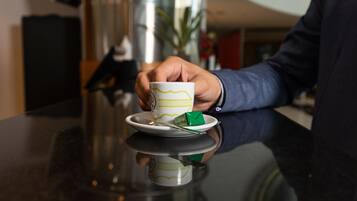 Una mano sosteniendo una taza con un diseño verde sobre un platillo, sobre una superficie reflectante.