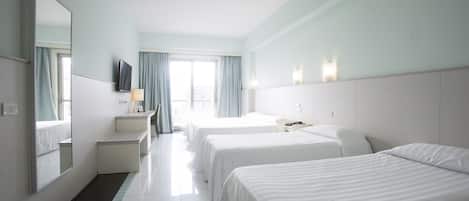 A hotel room with three beds, a TV, a desk, and a window with curtains.