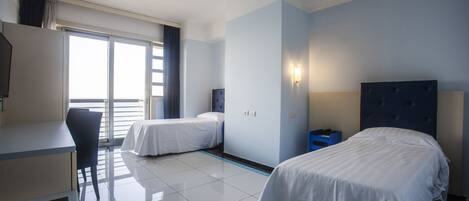 A hotel room with two beds, a desk, a chair, and a large window.