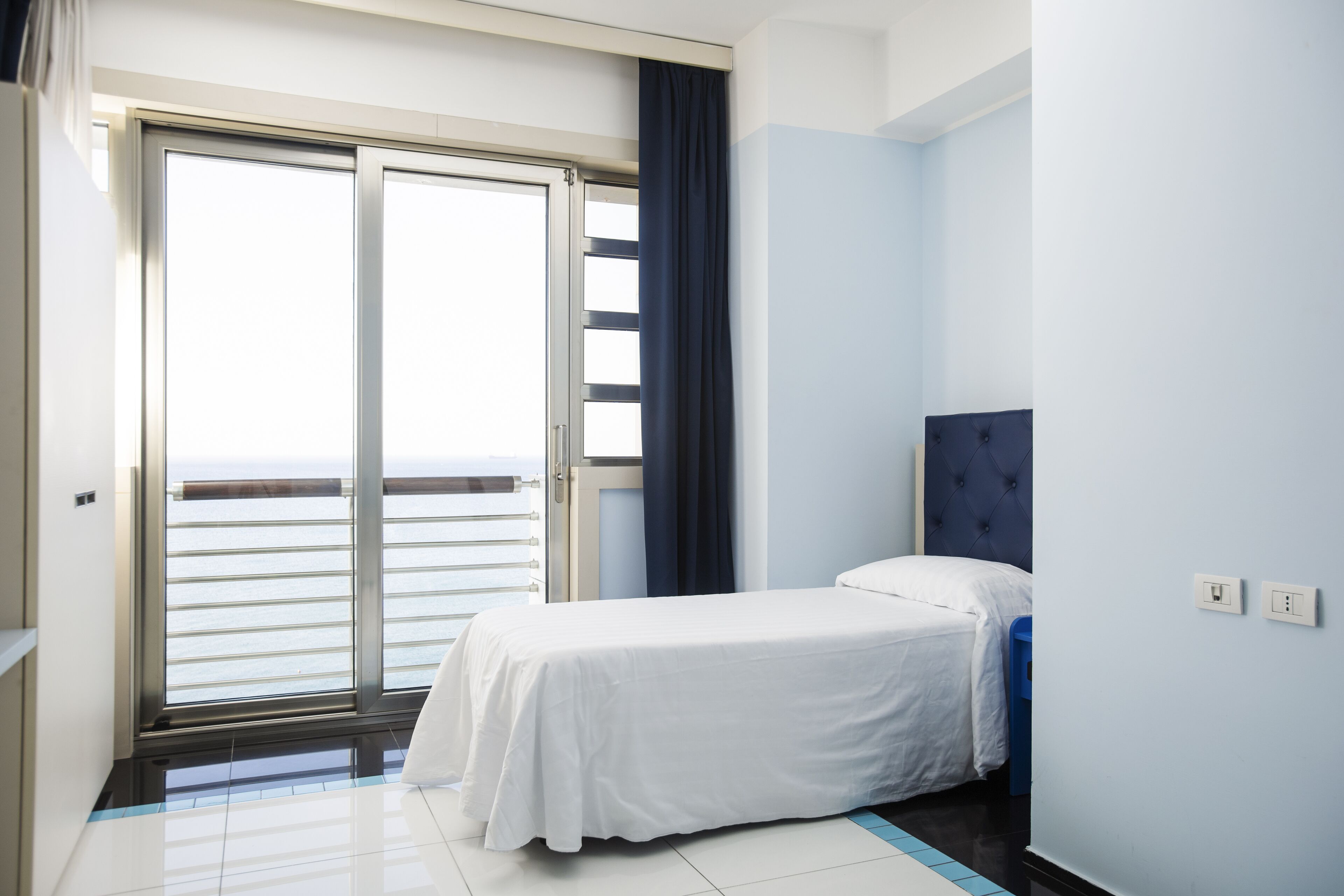 Habitación de hotel con cama, vista al mar a través de una puerta corredera y una pared de acento azul.