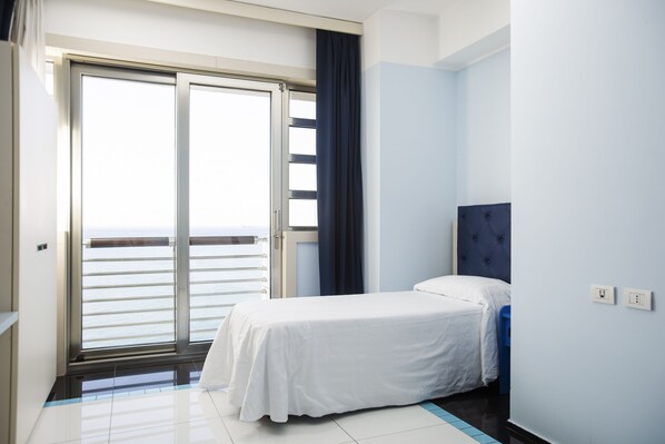 A hotel room with a bed, a view of the sea through a sliding door, and a blue accent wall. - Grand Hotel Salerno (Salerno)