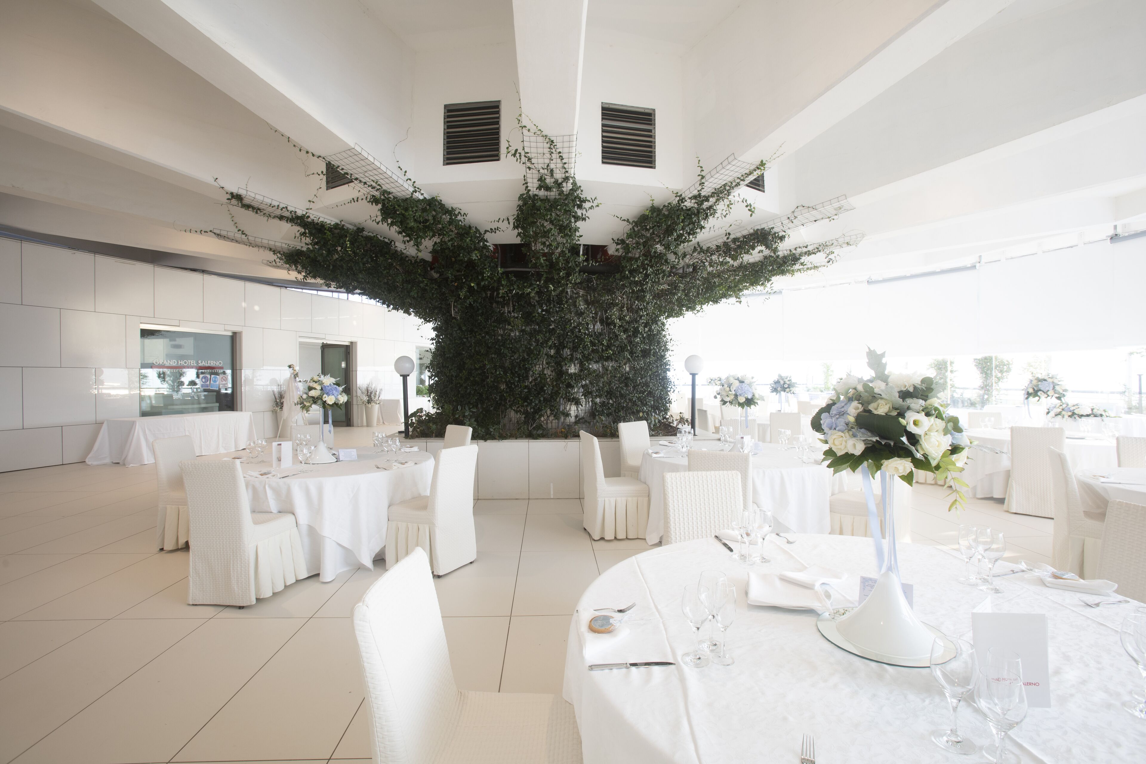 A spacious indoor venue with round tables set for dining, surrounded by white chairs.