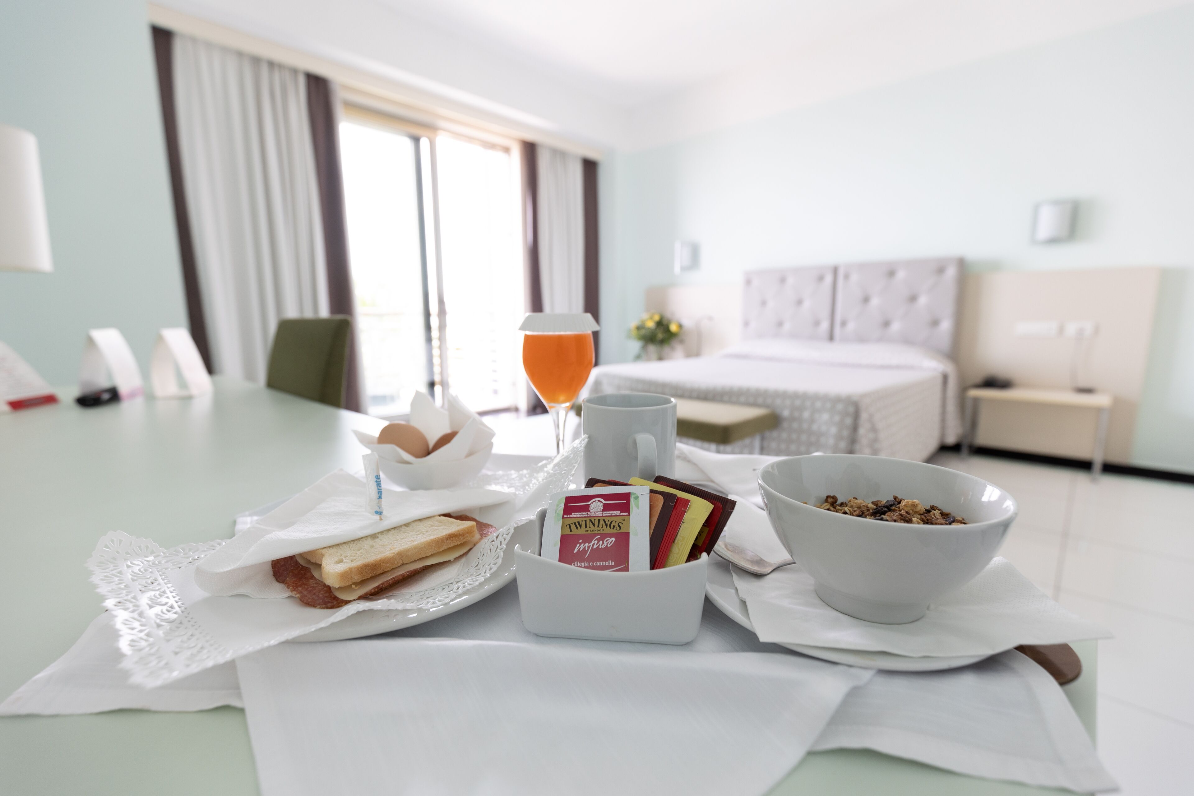 Habitación de hotel con una mesa de desayuno dispuesta con tostadas, una taza, un bol de cereales y bolsitas de té Twinings.