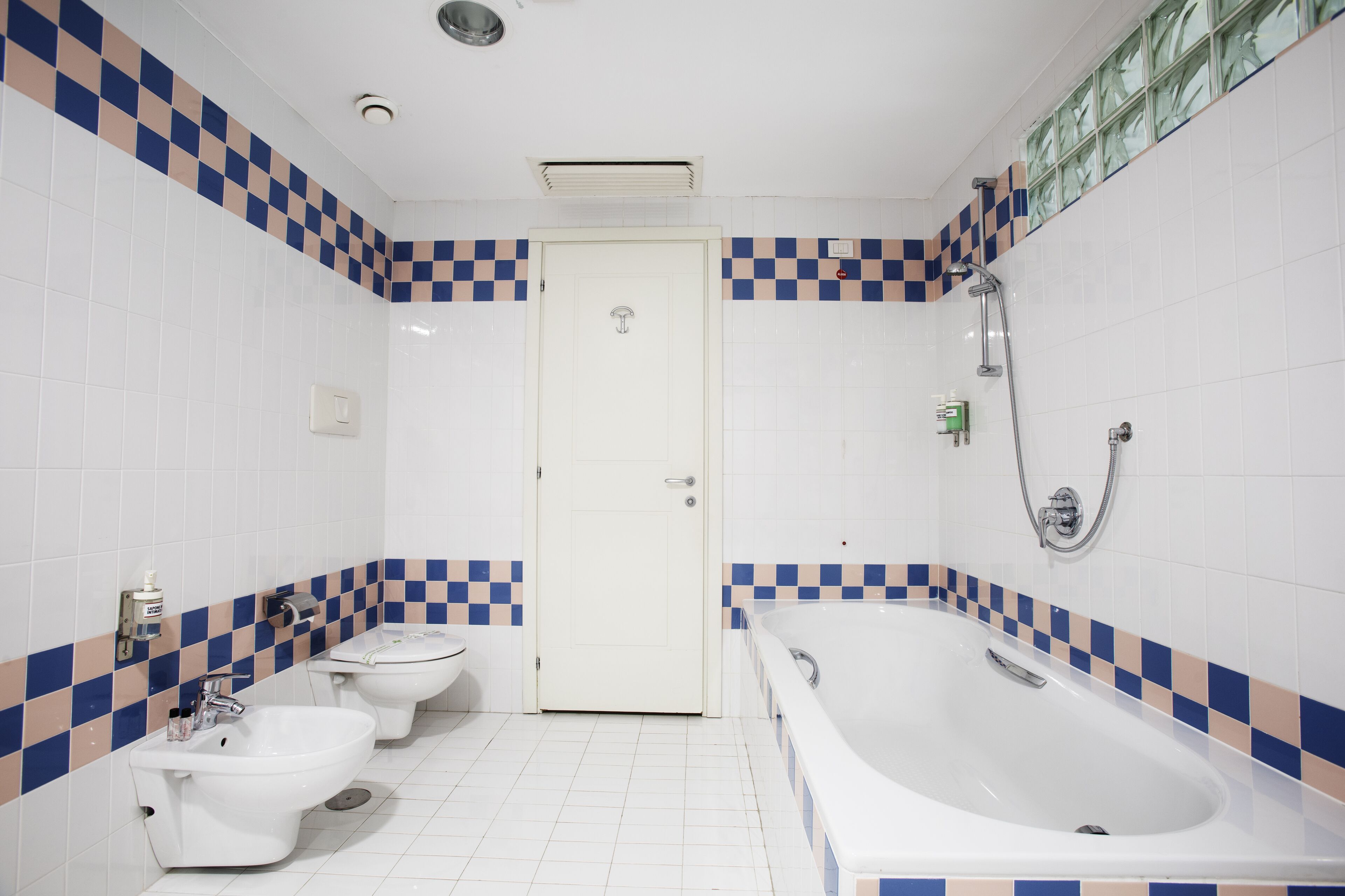 Een badkamer met een zwart-wit betegelde vloer, een toilet, een bidet en een bad.