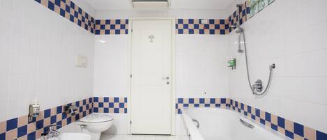 Een badkamer met een zwart-wit betegelde vloer, een toilet, een bidet en een bad.