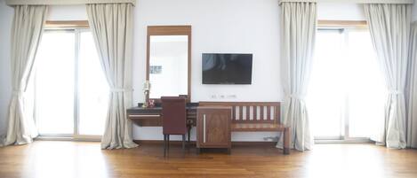 A room with a wooden desk, a chair, a television mounted on the wall, and a bench.