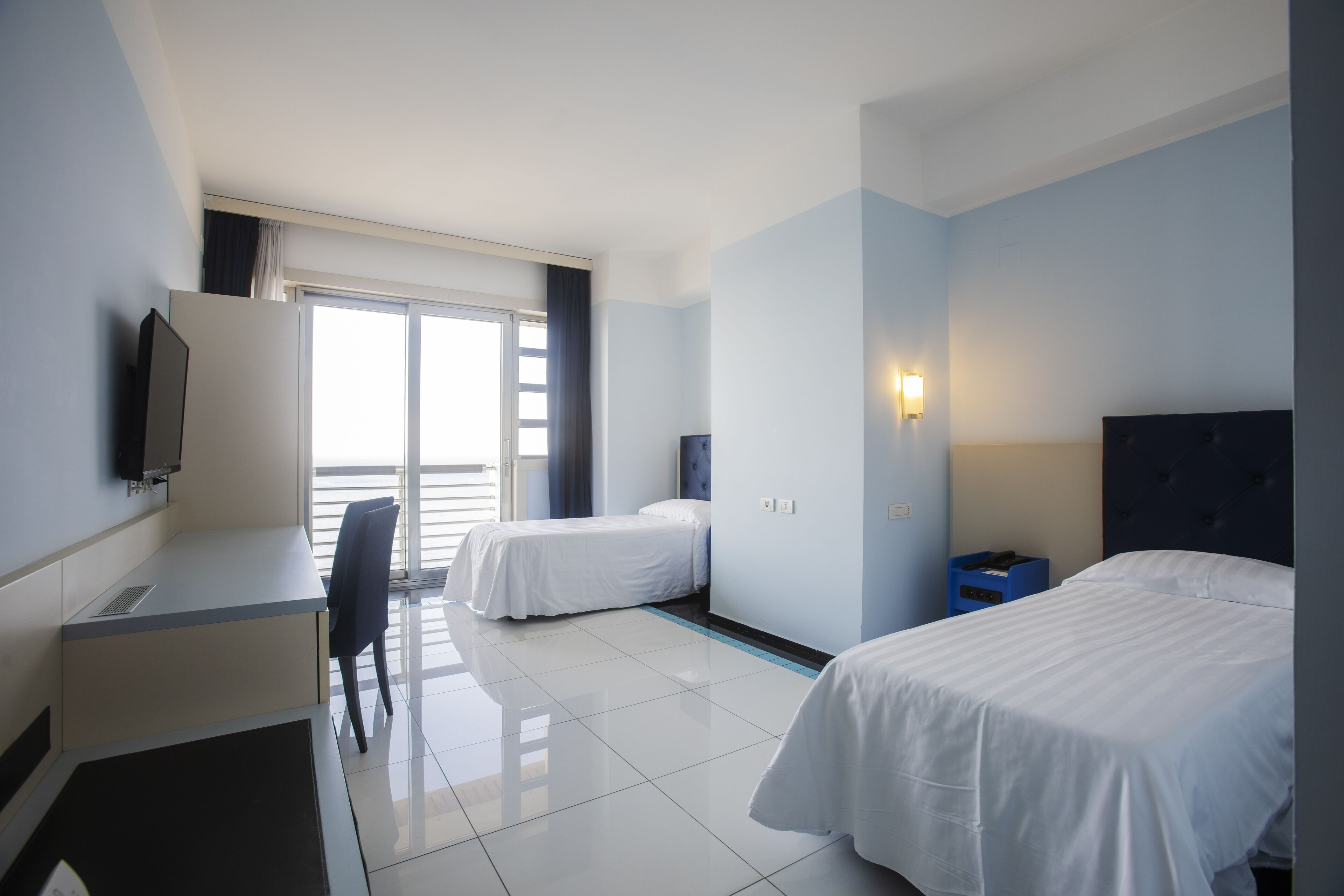 Ein Hotelzimmer mit zwei Betten, einem Schreibtisch, einem Stuhl, einem Fernseher und einem Fenster mit Vorhängen.
