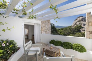Un balcon avec une table en bois et des chaises blanches, un mur en pierre et une vue sur un paysage montagneux.