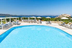 Un espace aménagé au bord de la piscine, avec des chaises longues et des parasols, offrant une vue panoramique sur la mer et les collines.
