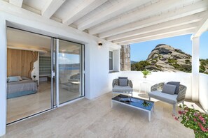 Een modern interieur met een glazen deur naar een slaapkamer, een balkon met zitplaatsen en uitzicht op rotsachtig terrein.