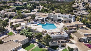 Een resort met een centraal gelegen zwembad, gebouwen van natuursteen en een bergachtige achtergrond.