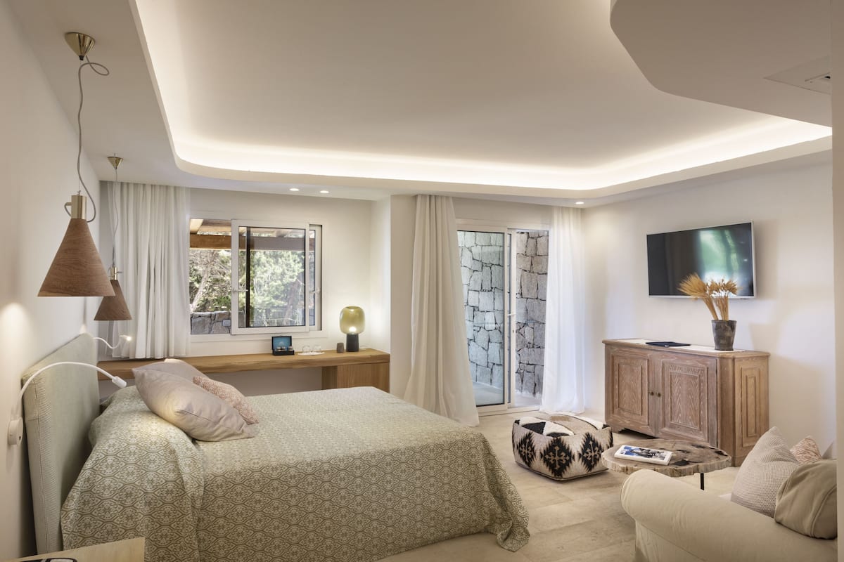 Een moderne slaapkamer met een bed, nachtkastje, lamp, televisie en uitzicht op het landschap.