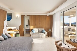 Una habitación de hotel moderna con cama, sofá, mesa de comedor y balcón con vistas.