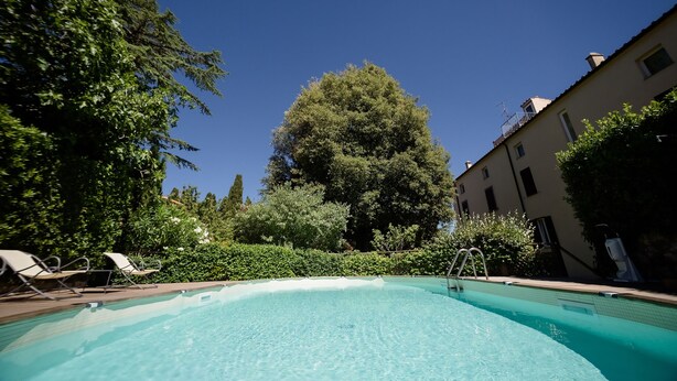 Una piscina cristalina con sillas de descanso, rodeada de vegetación y edificios.
