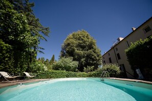 A clear swimming pool with lounge chairs, surrounded by greenery and buildings.