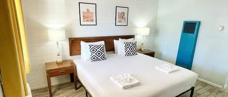 Habitación de hotel con una cama, dos mesitas de noche, un calentador de pared y una ventana con cortinas.