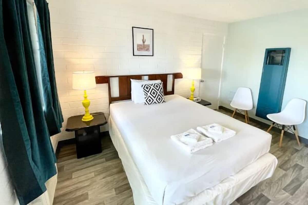 Hotellihuone, jossa on suuri sänky, kaksi yöpöytää valaisimineen, tuoli ja ovi.