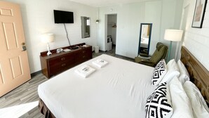 A hotel room with a bed, a dresser, a television, a mirror, a chair, and a lamp. - The Postcard Motel (Seligman)