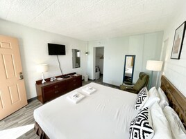 A hotel room with a bed, a dresser, a television, a mirror, a chair, and a lamp.