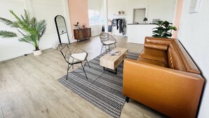 A spacious living area with a brown leather sofa, two wicker chairs, a coffee table, and a large potted plant. - The Postcard Motel (Seligman)