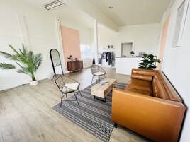 A spacious living area with a brown leather sofa, two wicker chairs, a coffee table, and a large potted plant.