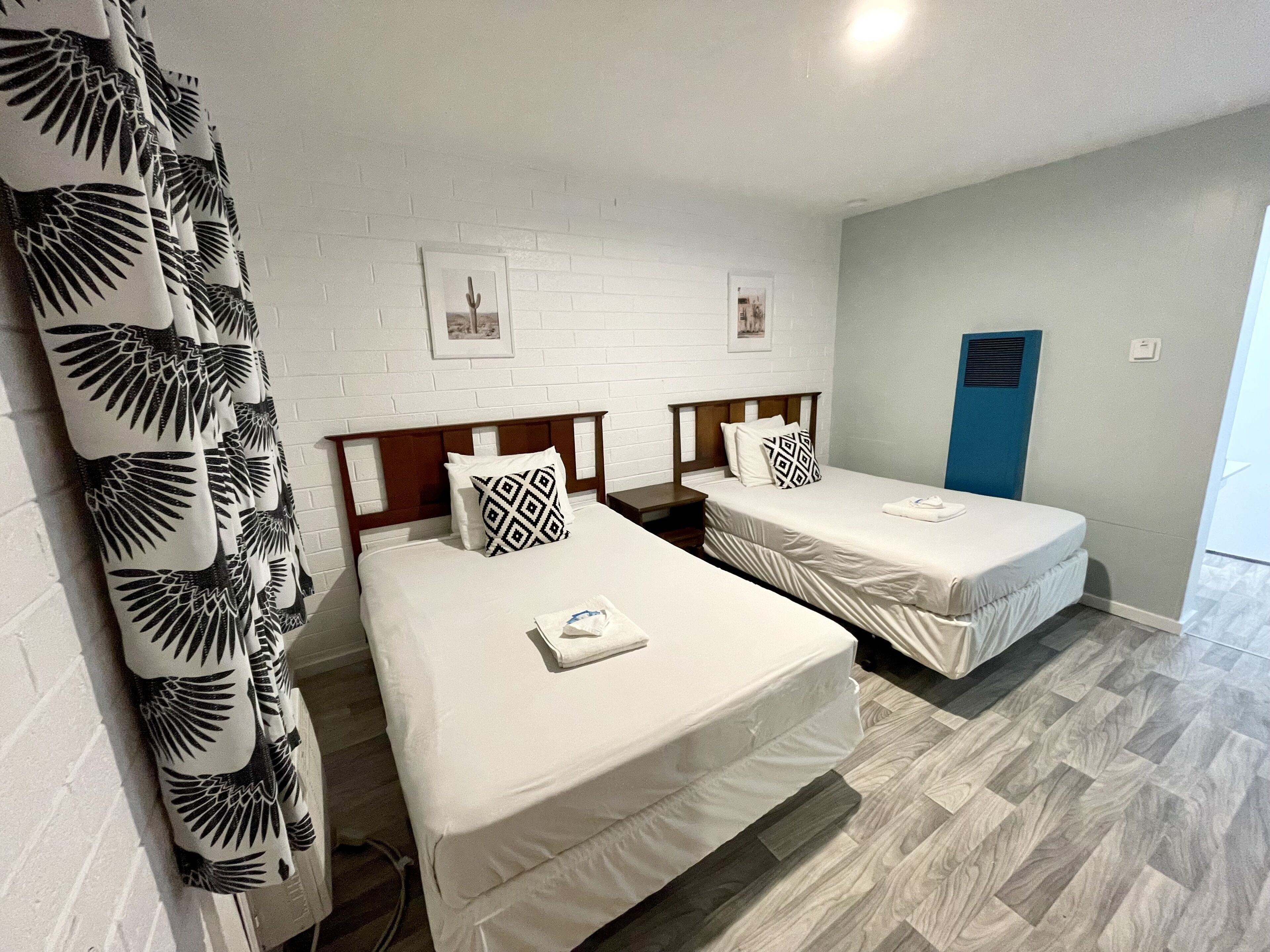 Habitación de hotel con dos camas, paredes blancas y suelo de madera.
