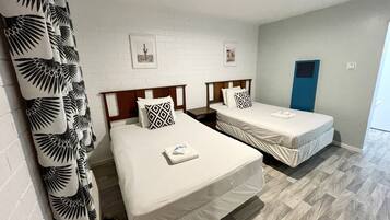 Habitación de hotel con dos camas, paredes blancas y suelo de madera.