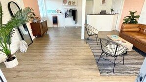 A spacious living area with a wooden floor, a sofa, a dining table with chairs, and a kitchen area in the background. - The Postcard Motel (Seligman)