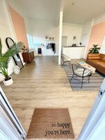 A spacious living area with a wooden floor, a sofa, a dining table with chairs, and a kitchen area in the background.
