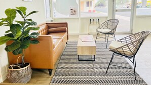 A modern living room with a leather sofa, two wireframe chairs, a coffee table, and a large potted plant. - The Postcard Motel (Seligman)