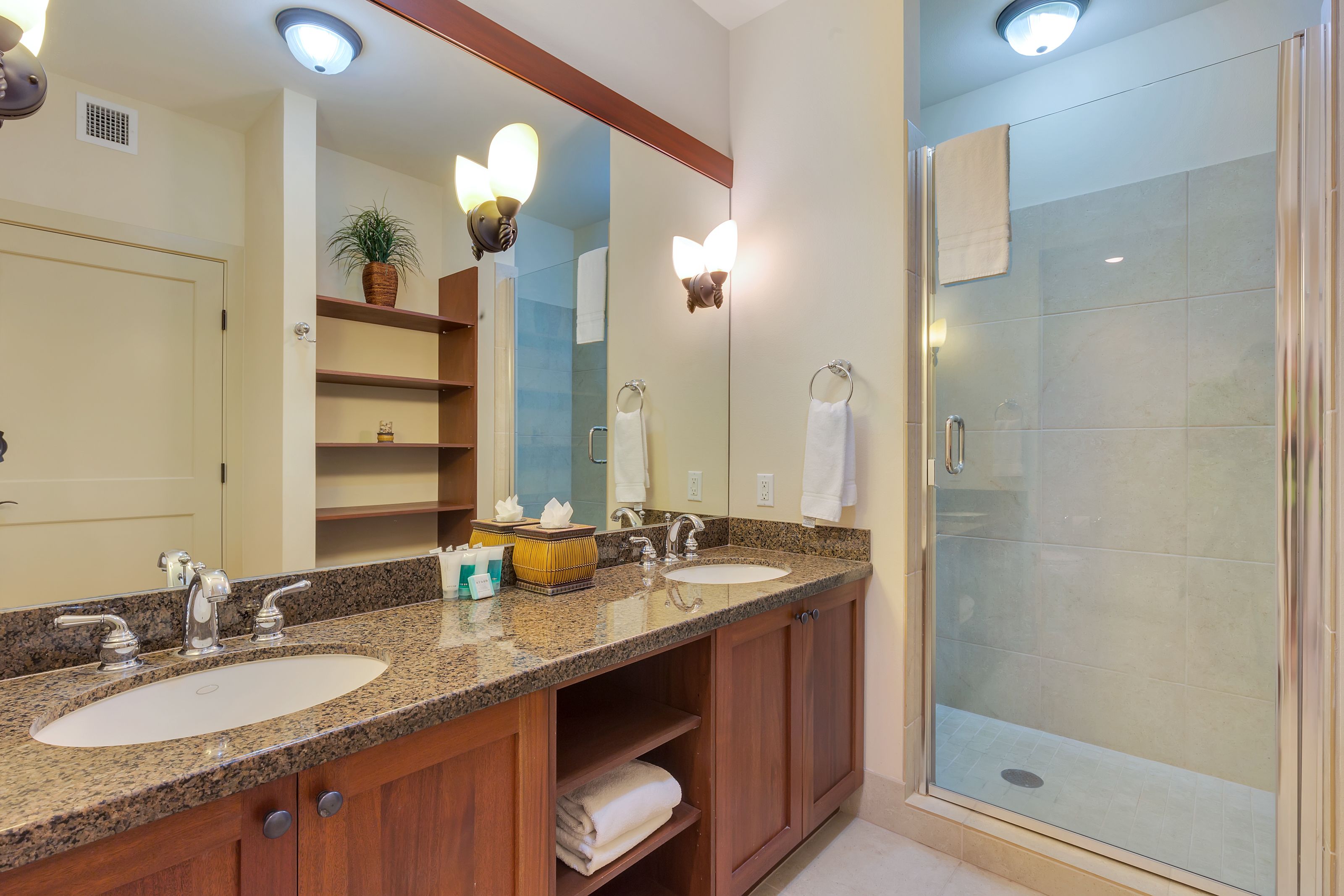 A bathroom with two sinks, a large mirror, and a glass-enclosed shower.