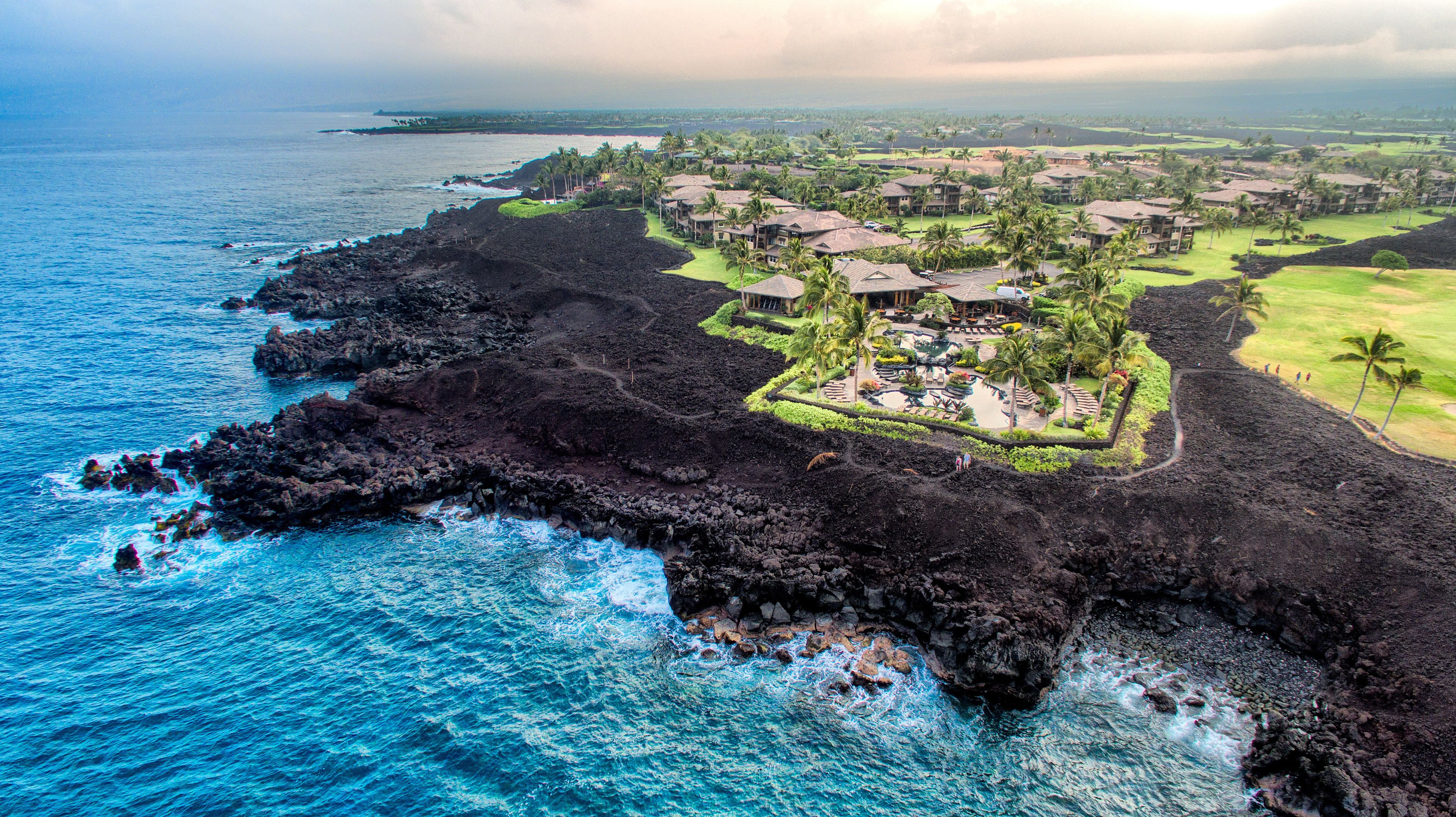 An aerial view of a coastal resort with a rocky shoreline, a pool area, and multiple buildings.