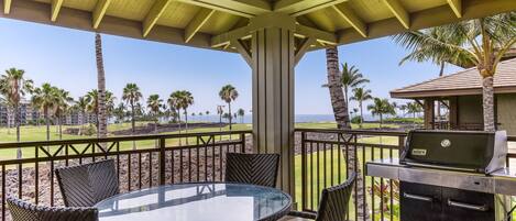 A covered outdoor area with a round table and chairs, a grill, and a view of a golf course and ocean.