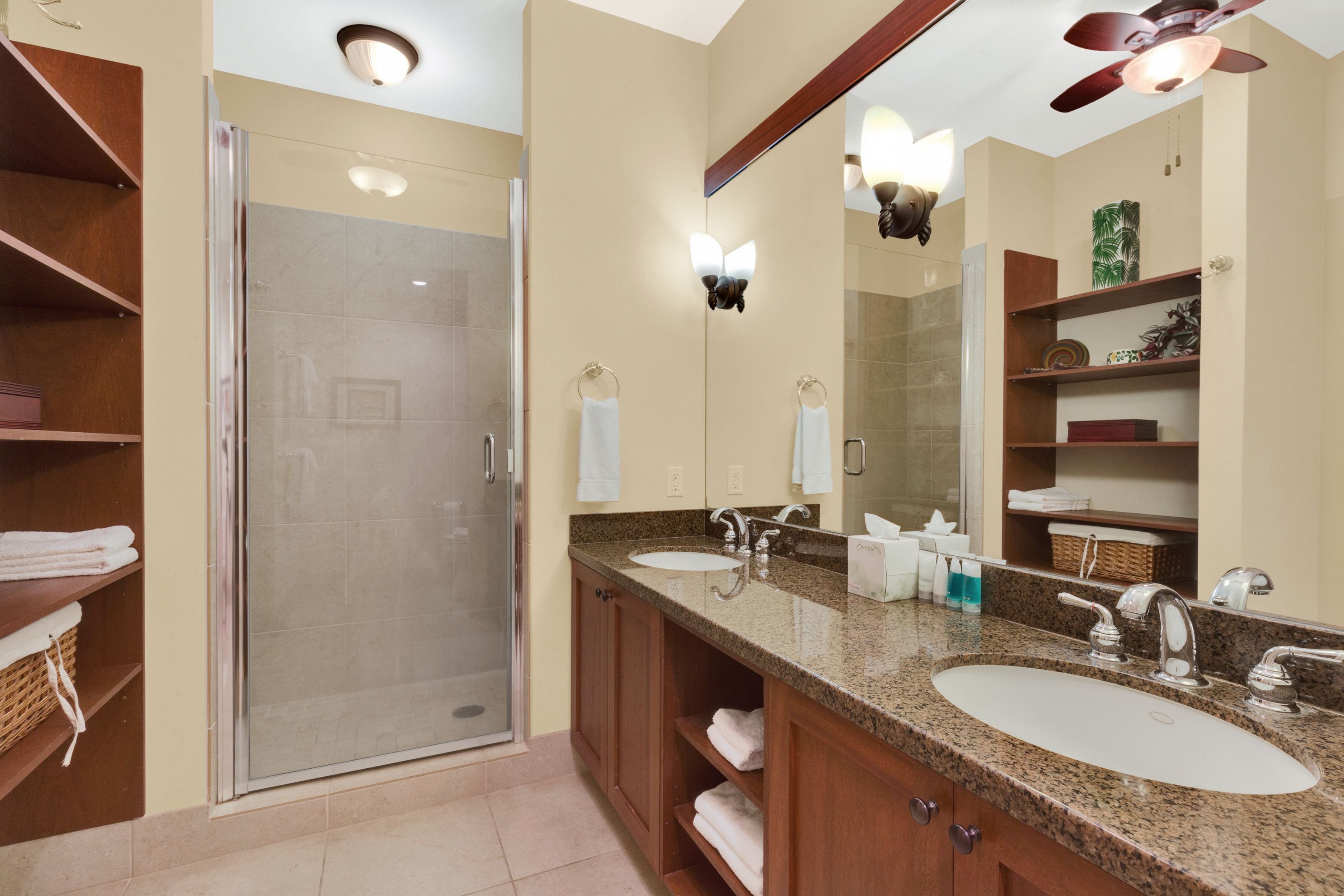 A modern bathroom with a glass-enclosed shower, two sinks, and wooden shelving.
