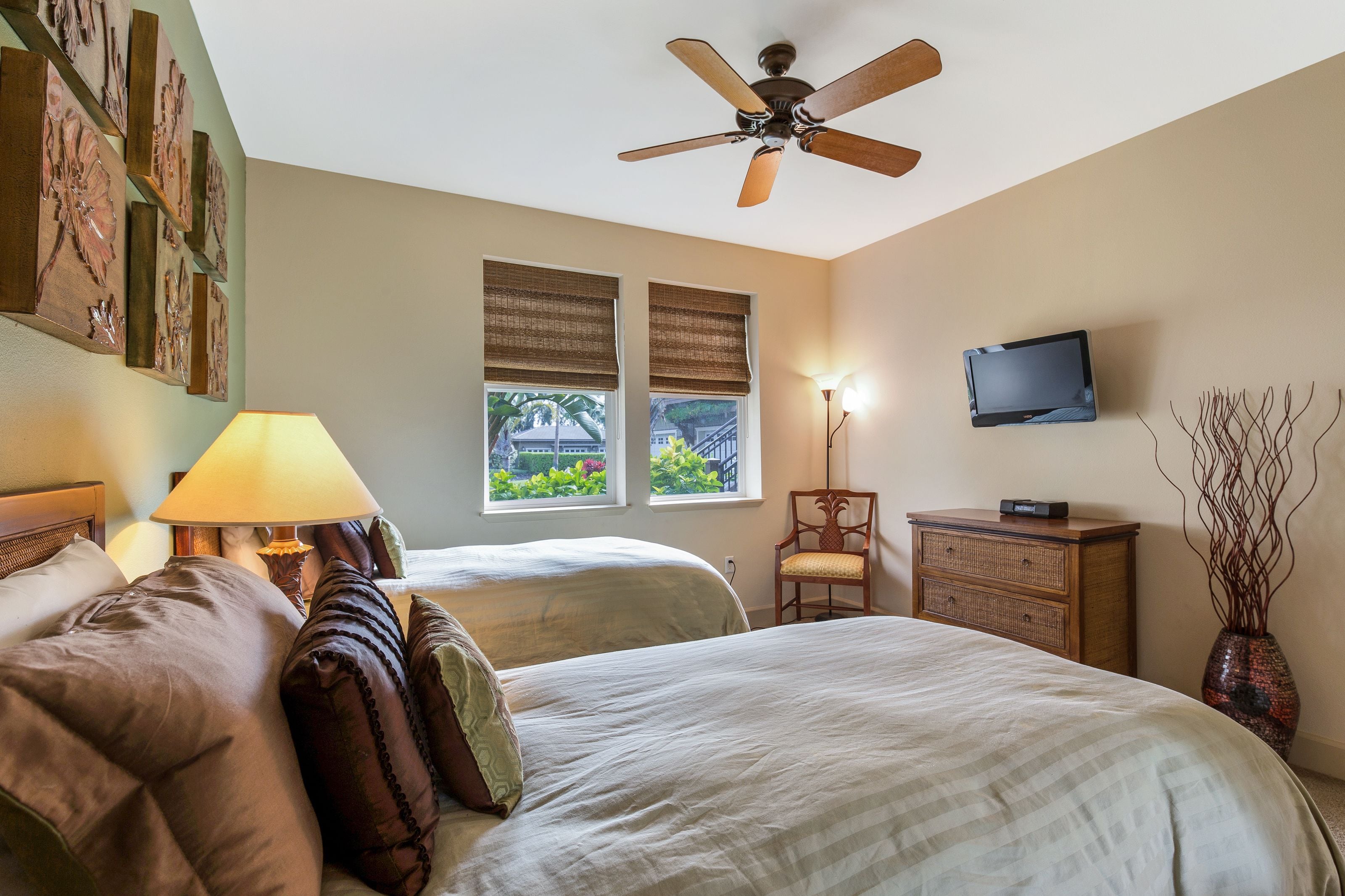 Une chambre d’hôtel avec deux lits, un ventilateur de plafond, une télévision, une lampe et une fenêtre donnant sur un paysage verdoyant.