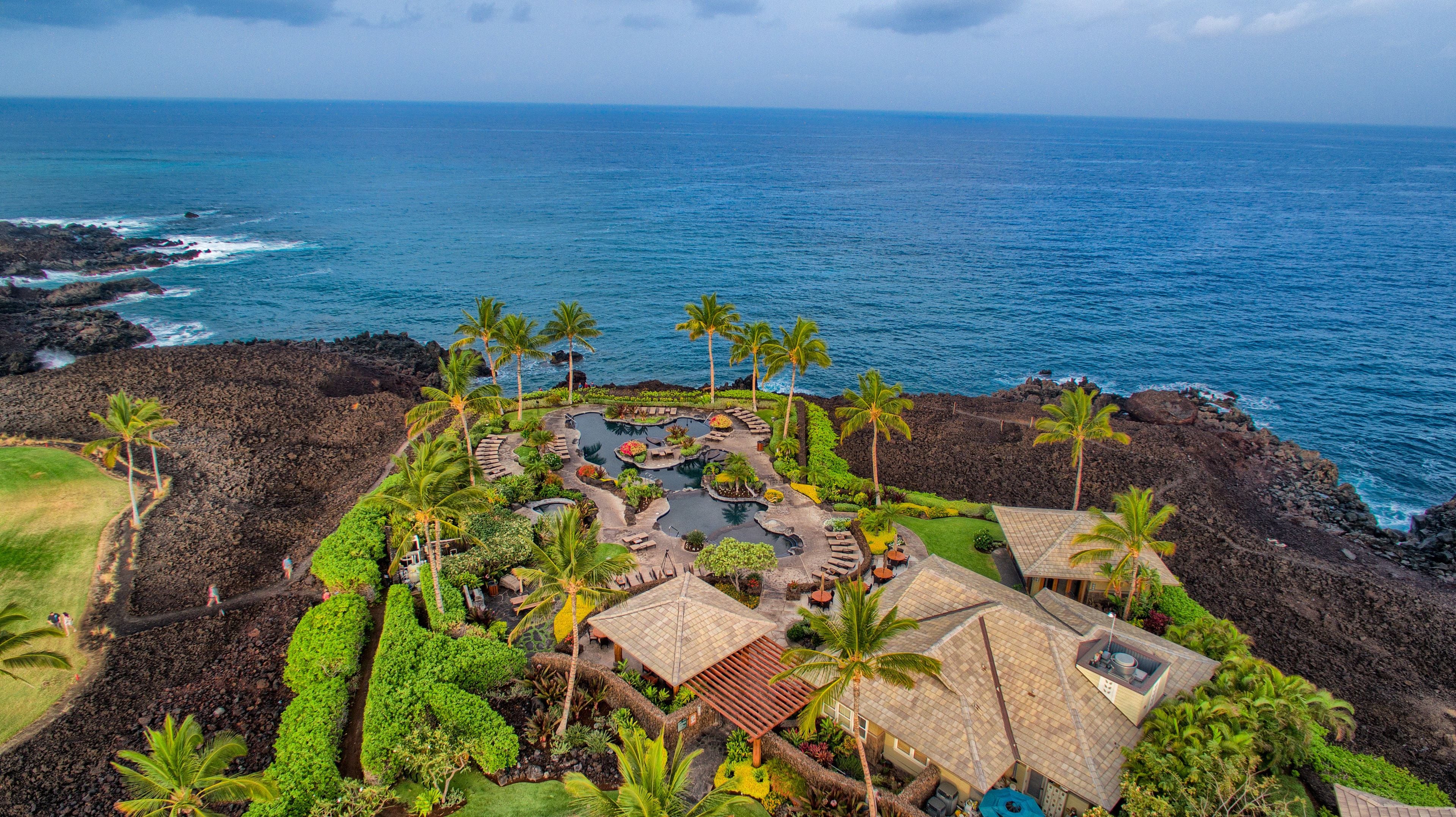 A resort with a central pool area, multiple lounge areas, and a view of the ocean.