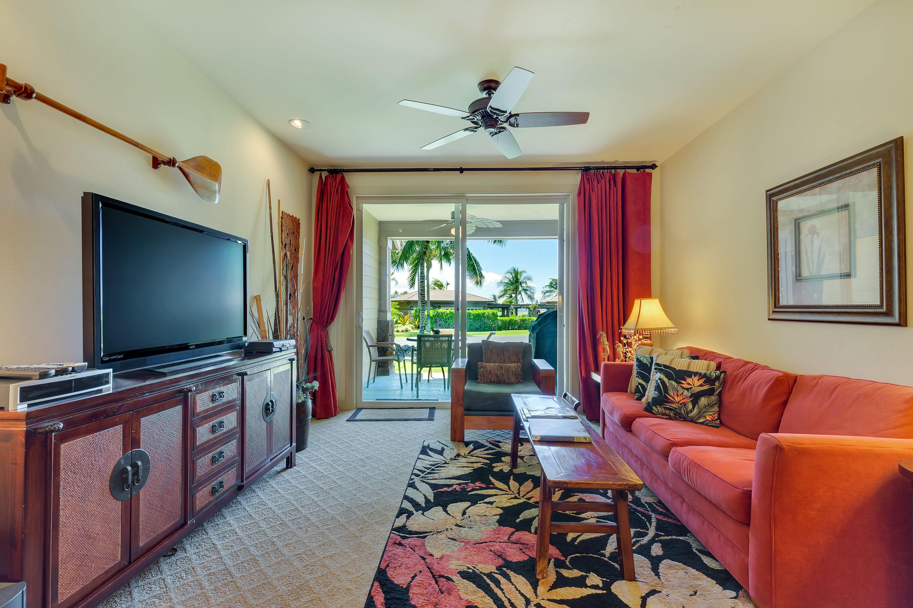 A living room with a flat-screen TV, a sofa, a coffee table, and a ceiling fan.
