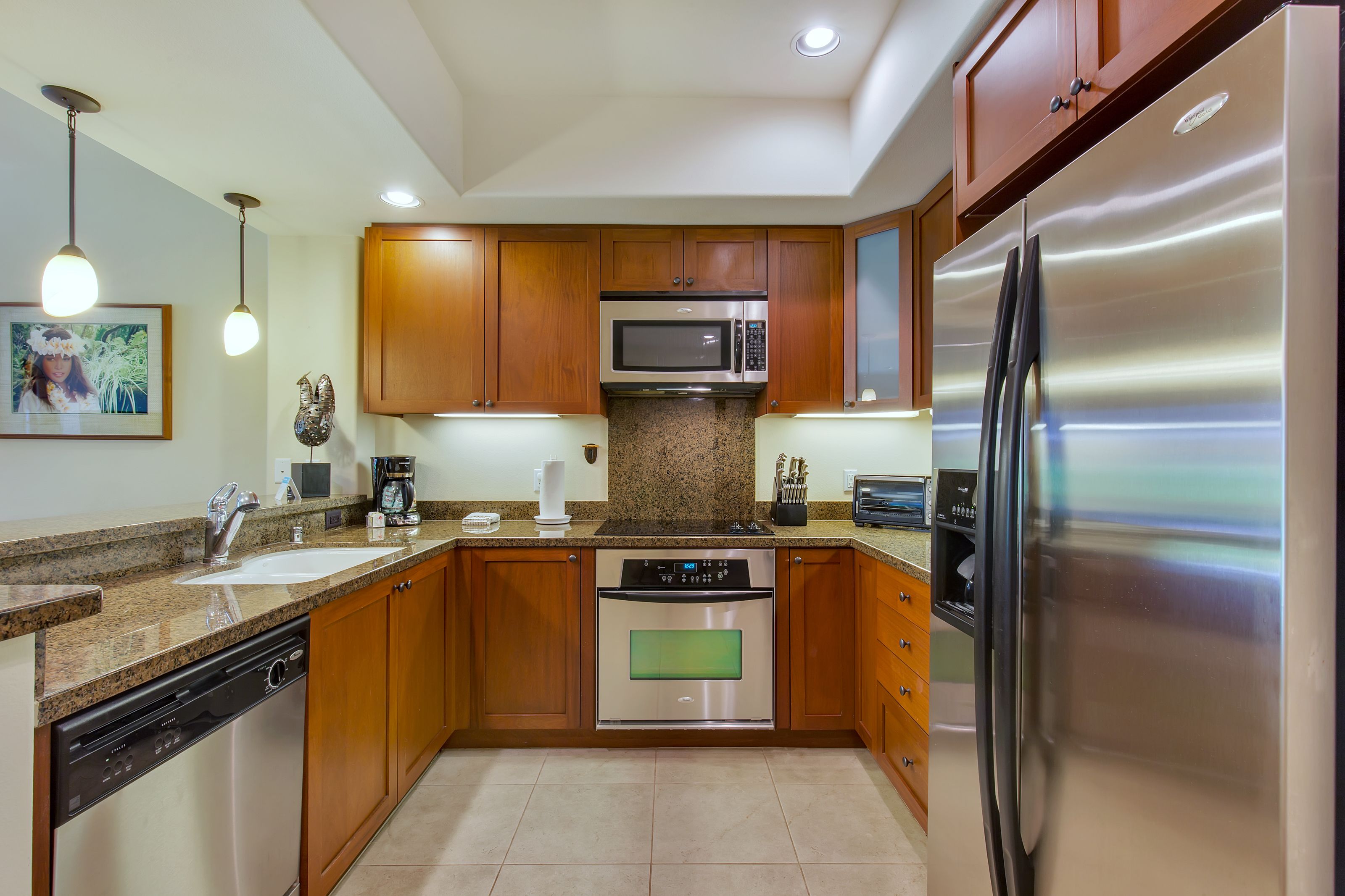 Una cocina moderna con armarios de madera, electrodomésticos de acero inoxidable, encimeras de granito e iluminación colgante.
