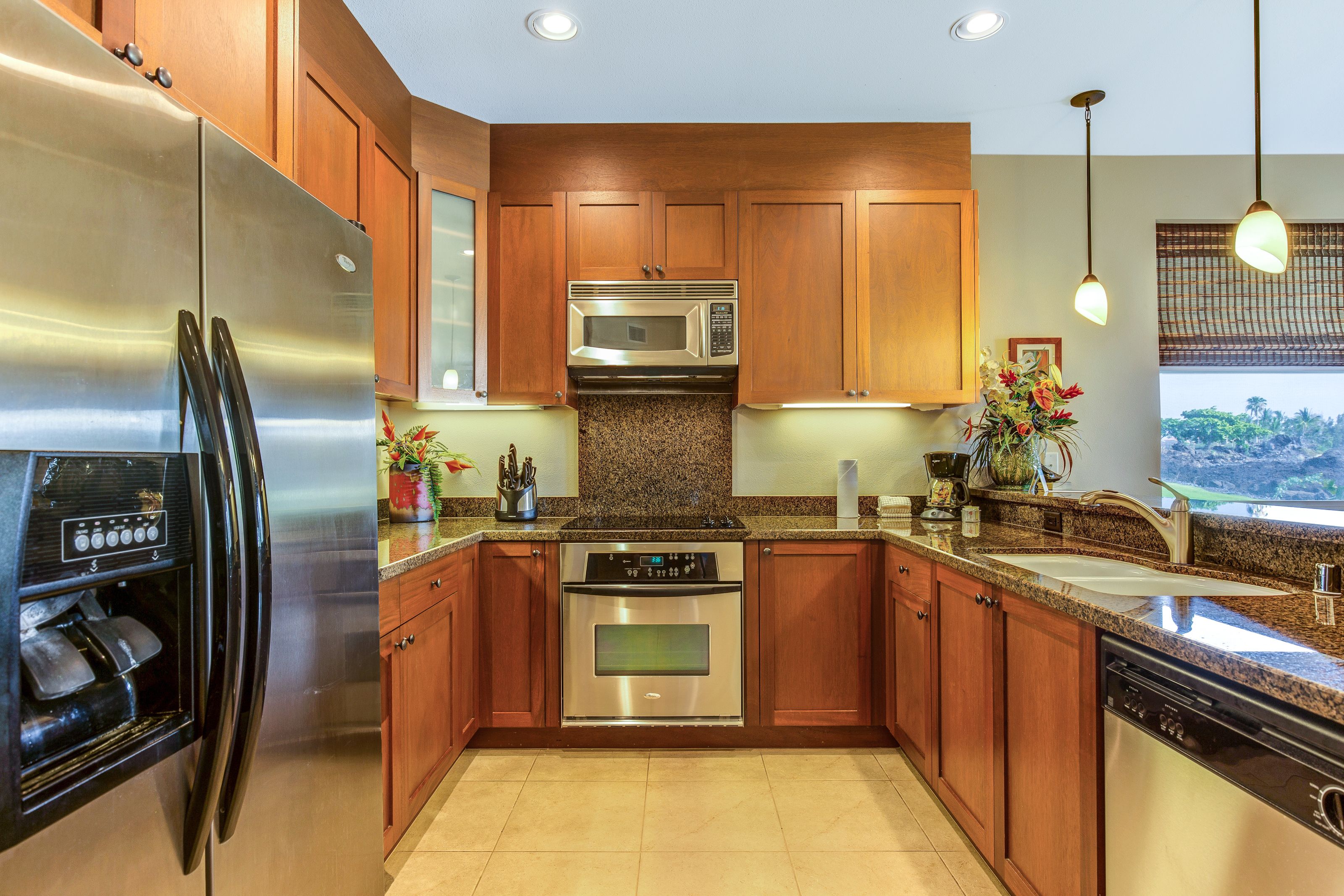 A modern kitchen with stainless steel appliances, wooden cabinets, granite countertops, and pendant lighting.