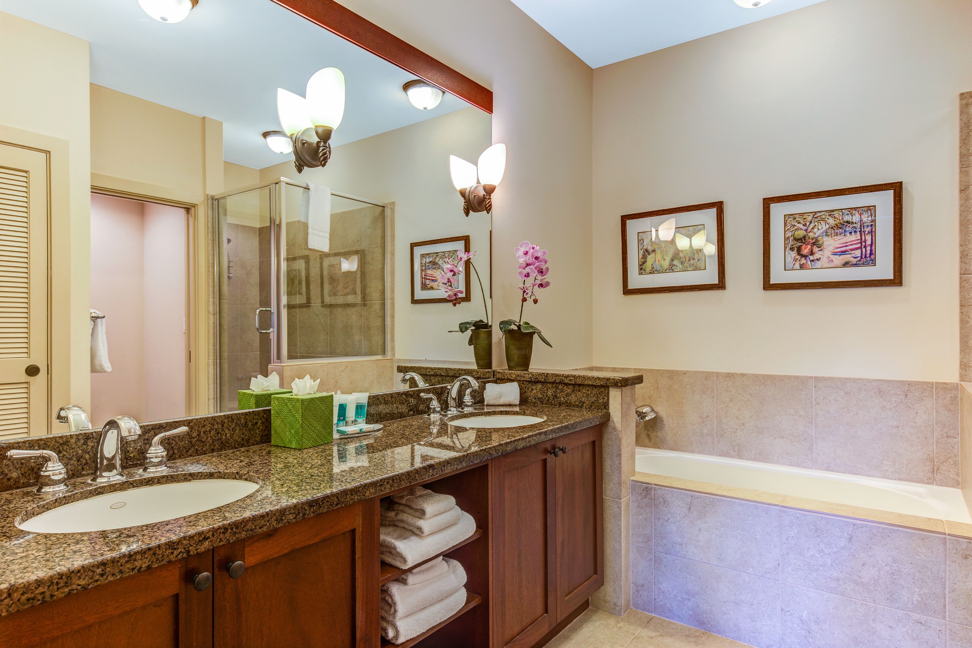 Un baño con lavamanos de encimera de granito, un espejo grande y una bañera.