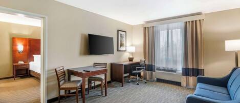 Habitación de hotel con cama, escritorio, silla, televisor y ventana con cortinas.