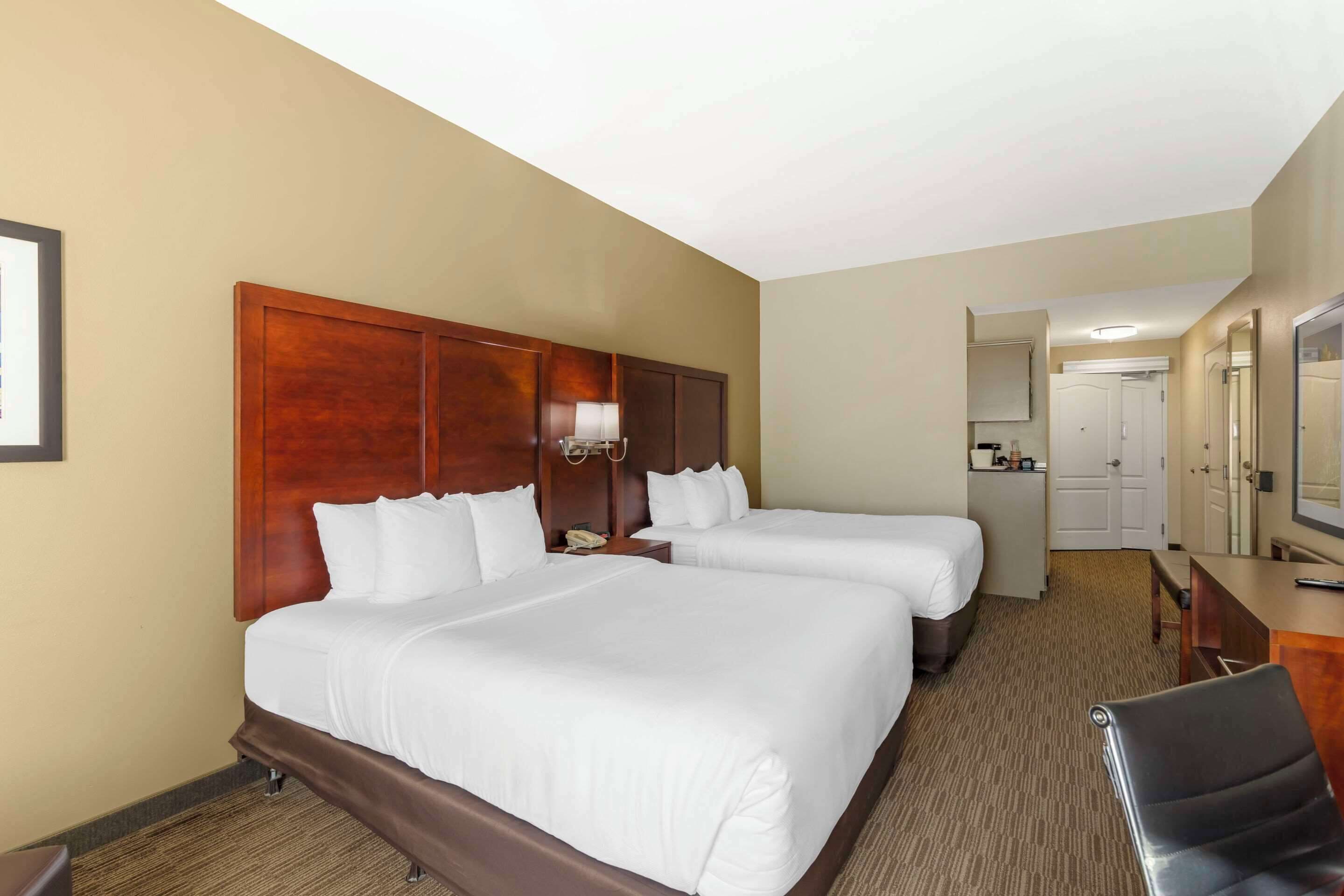 Une chambre d’hôtel avec deux lits, un bureau, une chaise, un miroir et une porte donnant sur une salle de bain.