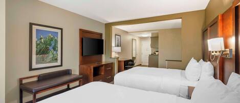 A hotel room with two beds, a TV, a bench, a desk, and a mirror.