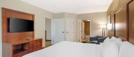 A hotel room with a large bed, a TV mounted on a wooden cabinet, a desk with a chair, and a bathroom visible through an open door.