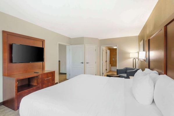 A hotel room with a large bed, a TV mounted on a wooden cabinet, a desk with a chair, and a bathroom visible through an open door.