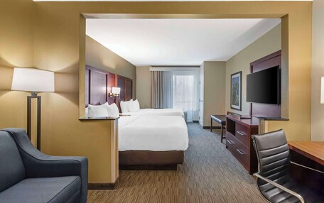 A hotel room with a large bed, a desk, a chair, a TV, and a window with curtains.