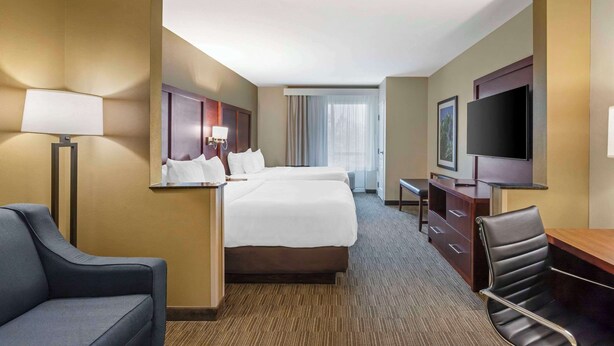 A hotel room with a large bed, a desk, a chair, a TV, and a window with curtains.