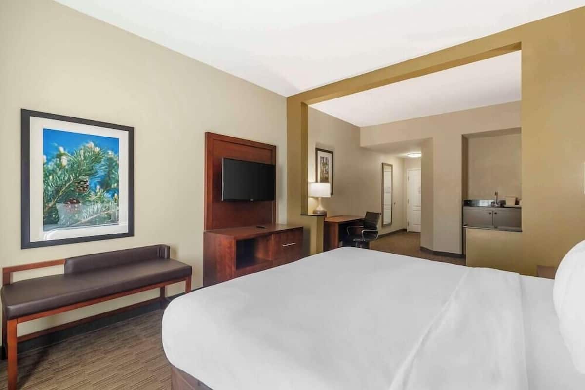 A hotel room with a large bed, a bench, a TV, a desk, and a bathroom visible in the background.